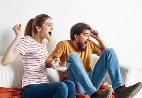 interested woman and bearded man sit on the couch popcorn in a plate and flower in a pot photo