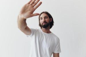 Happy adult man with a beard smiles and pulls the cook into the camera listening to music in headphones in a distressed t-shirt on a white isolated background photo