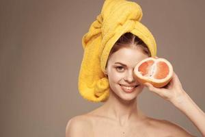 alegre mujer con un amarillo toalla en su cabeza desnudo espalda pomelo en mano natural productos cosméticos foto