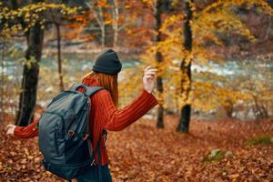 mujer caminante con mochila en otoño bosque cerca montaña río y caído hojas foto