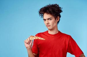 man holding a slice of pizza in his hand and curly hair red t-shirt blue background photo