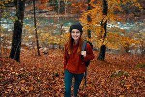 a traveler in a red sweater and a hat walks in the autumn forest near a mountain river top view photo