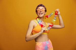 Woman with floral Hawaiian wreath around her neck has fun dancing and smiling in bright clothing against an orange background photo