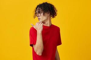 Shocked funny Caucasian young man in red t-shirt point finger aside posing isolated on over yellow studio background. The best offer with free place for advertising. Emotions for everyday concept photo