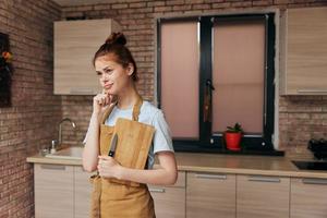 bonito mujer en un marrón delantal corte tablero cocina interior inalterado foto