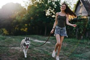 Woman and her husky dog happily running through the grass in nature in the park smile with teeth fall walk with pet, traveling with a dog friend photo