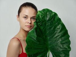 a woman in a red t-shirt on a light background holds a green leaf in her hands field natural look photo
