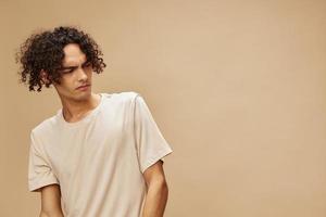 Unhappy discontented awesome tanned curly man in basic t-shirt with disgust looks aside posing isolated on beige background. Fashion New Collection offer. People Emotions concept. Free place for ad photo