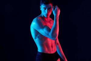 sexy guy with athletic physique posing on a black background and holds his hand near his face photo