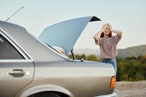 un mujer tristemente mira dentro el abierto maletero de un coche durante un detener en el la carretera en el camino a naturaleza. foto