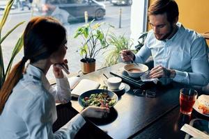 un hombre y un mujer en un camisa teniendo cena a un mesa en un restaurante interior en el antecedentes caliente comida bebidas foto