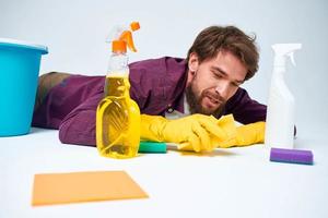 A man lies on the floor with a bucket of detergents providing services light background photo