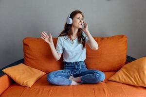 pretty woman listening to music with headphones on the orange sofa apartments photo