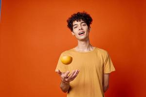 Cheerful curly guy in a yellow t-shirt oranges in his hands red background photo