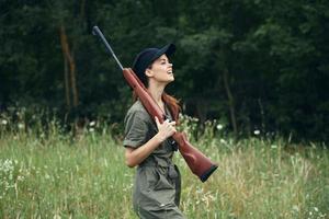 Woman on outdoor Side view of holding a weapon in the hands of a green jumpsuit black cap photo