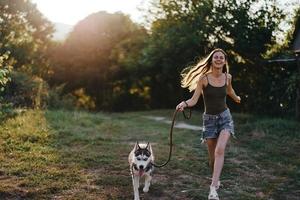 un mujer carreras con un perro en el bosque durante un noche caminar en el bosque a puesta de sol en otoño. estilo de vida Deportes formación con tu amado perro foto