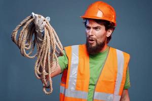 A bearded man construction worker in an orange hard hat safety rope in his hands photo