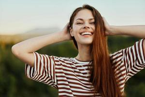 Close-up portrait of a young woman with a beautiful smile with teeth in a striped t-shirt against the background of trees photo