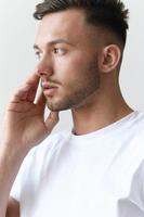 Portrait shot of handsome pensive romantic serious tanned man guy in basic t-shirt looks aside posing on white background. Fashion Style New Collection Offer. Copy space for ad. Model snap photo