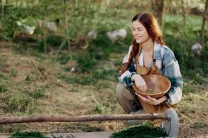 A woman farmer smiles and pours food for the birds into a bird feeder from a bowl at an outdoor farm to raise healthy, organic chickens photo