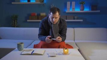 The man is sick with a cold at home. Natural gas was cut off.  Man using candle light for heating and lighting calculates high priced bills. video