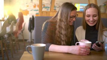 Two friends woman in cafe using mobile phone and have fun communicating video