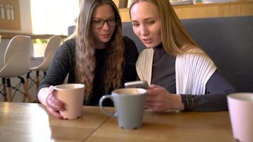 Two friends woman in cafe using mobile phone and have fun communicating video