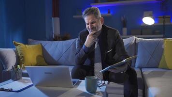 Smart positive man using laptop while sitting on sofa at home.  Mature businessman working remotely at home working late at night, sleepy, overtime. video