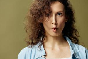 Funny cute curly beautiful female in jeans casual shirt makes lips bow like fish posing isolated on over olive green pastel background. Being Yourself. People Lifestyle emotions concept. Copy space photo
