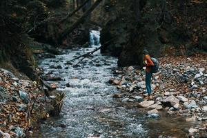 mujer en el montañas cerca el río con un mochila en su espalda y un bosque en el antecedentes foto