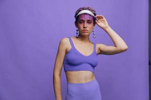 Portrait of a sporty fashion woman posing in a purple sports suit for yoga and a transparent cap on a purple background monochrome photo