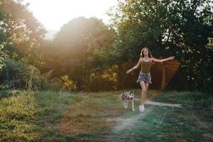 un mujer carreras con un perro en el bosque durante un noche caminar en el bosque a puesta de sol en otoño. estilo de vida Deportes formación con tu amado perro foto