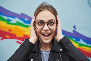 Happy woman in a leather jacket and glasses near the multicolored graffiti on the wall photo