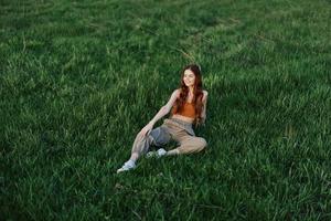 Female student freelancer sits on the grass in the park and watches the sunset, the concept of harmony with the world and nature photo