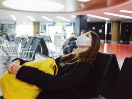 woman with closed eyes of a medical mask waiting for a flight at the airport photo