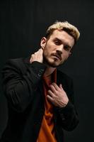 man in orange sweater and jacket on a dark background gesturing with his hands close-up cropped view photo