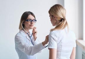 mujer limpieza dama en un médico vestido escucha a el del paciente latido del corazón en un ligero antecedentes foto