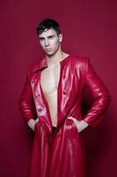 handsome male athlete brunette in a leather coat on a red background gay photo
