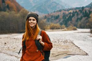 woman in a sweater hat with a backpack resting near the river in the mountains on nature landscape photo