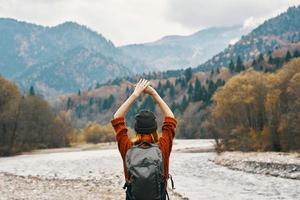 happy woman in the mountains travels near the river in nature and raised her hands up photo