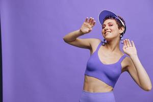 Sports fashion woman dancing posing smiling with teeth in a purple sports suit for yoga on a slender body and a transparent cap on her head on a purple background monochrome photo