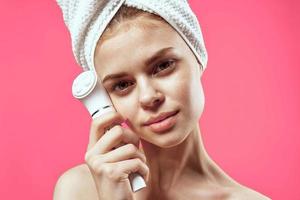 woman with towel on head cleaning face skin care pink background photo
