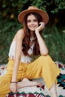 hermosa joven niña de cerca mira dentro el cámara en un sombrero vistiendo un eco hippie al aire libre, hermosa sonrisa con dientes en el puesta de sol ligero foto