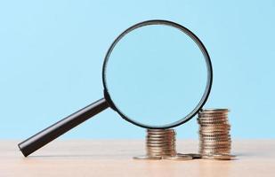 A stack of metal coins and a plastic magnifier on a blue background. The concept of increasing taxes, subsidies photo