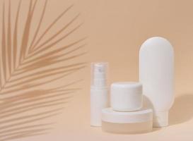 White plastic container tube, a jar with a lid for cosmetics on a beigebackground with a shadow from a palm leaf. Advertising and promotion photo