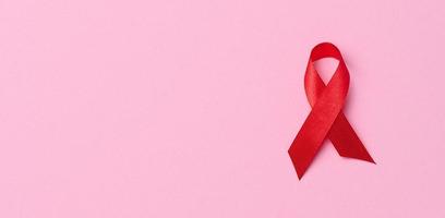 A silk red ribbon in the form of a bow on a pink background, a symbol of the fight against AIDS and a sign of solidarity and support photo