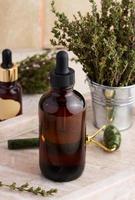 Thyme essential oil in glass bottle with dropper and fresh thyme sprigs on table, cosmetic ingredient photo