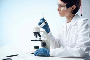 woman scientist in a white coat looking through a microscope study photo