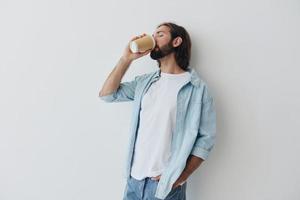 Lanza libre milenario hombre con barba Bebiendo café desde un cangrejo taza en elegante hipster ropa en un blanco antecedentes foto