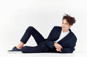 a man with curly hair lies in a suit on the floor in a bright room and sneakers style photo